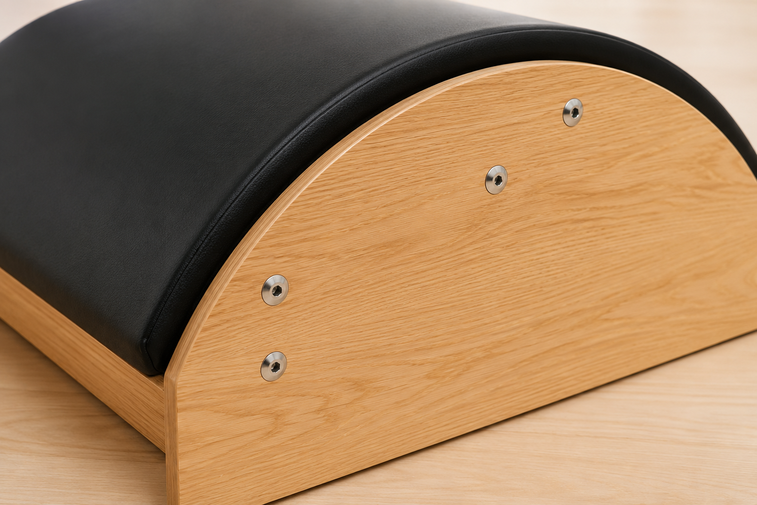 Close-up of a Pilates reformer machine showing the black padded arc and natural wood frame with metal screws on a light wood floor.
